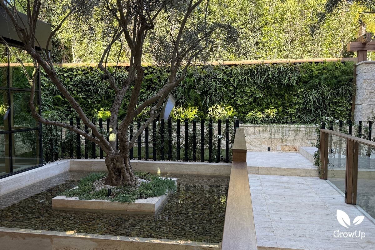 Large living greenwall in serene garden with a tree and water feature.
