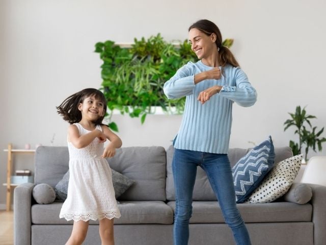 mother and daughter dancing at home in front of greenwall